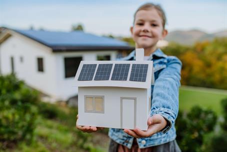 girl holding paper model of house with solar panels